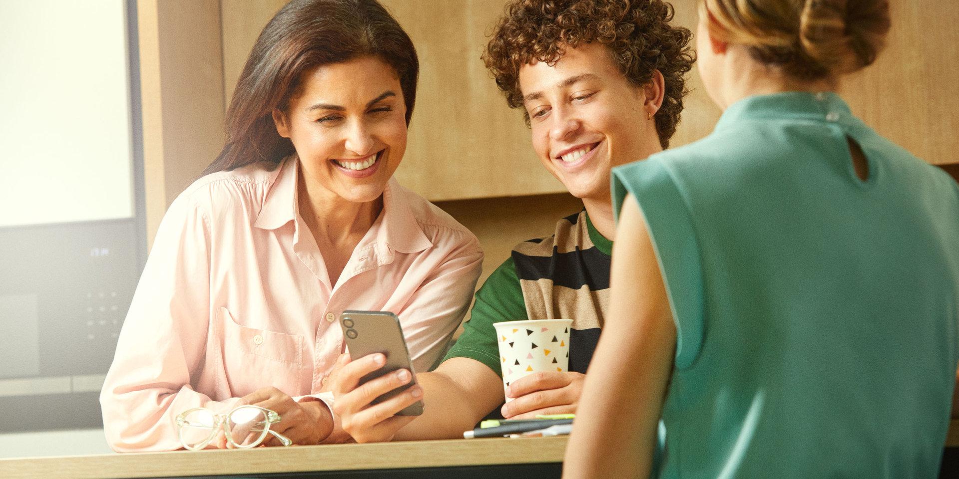 Eine erfahrene Kollegin und ein Lehrling bei Wüstenrot schauen gemeinsam auf sein Smartphone